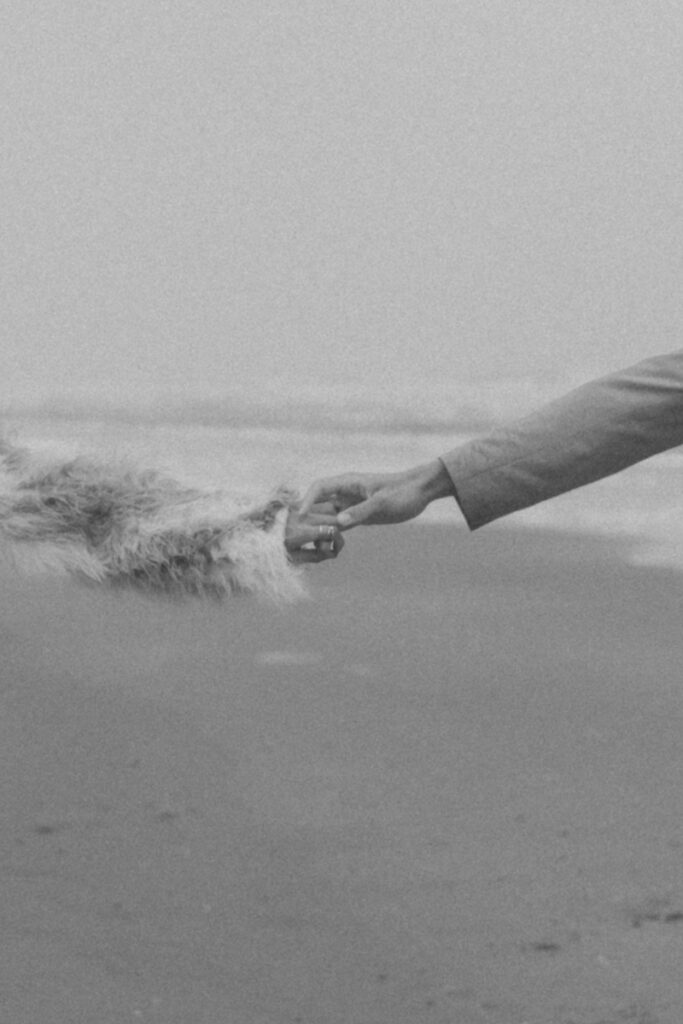 Schwarz-Weiß-Foto von zwei Händen, die sich am Strand berühren, symbolisiert Verbindung und Zärtlichkeit.