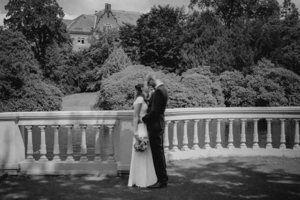 Schwarz-Weiß-Foto: Brautpaar küsst sich vor einer malerischen Kulisse im Schlossgarten Oldenburg
