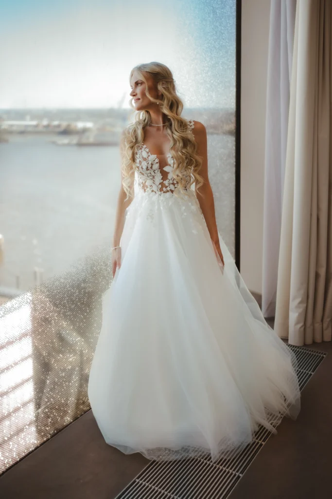 Braut in elegantem Hochzeitskleid mit Blick auf das Wasser in der Elbphilharmonie Hamburg.