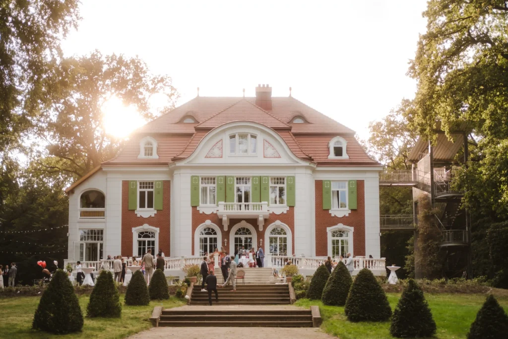 Historische Villa als Hochzeitslocation mit Gästen auf der Treppe.
